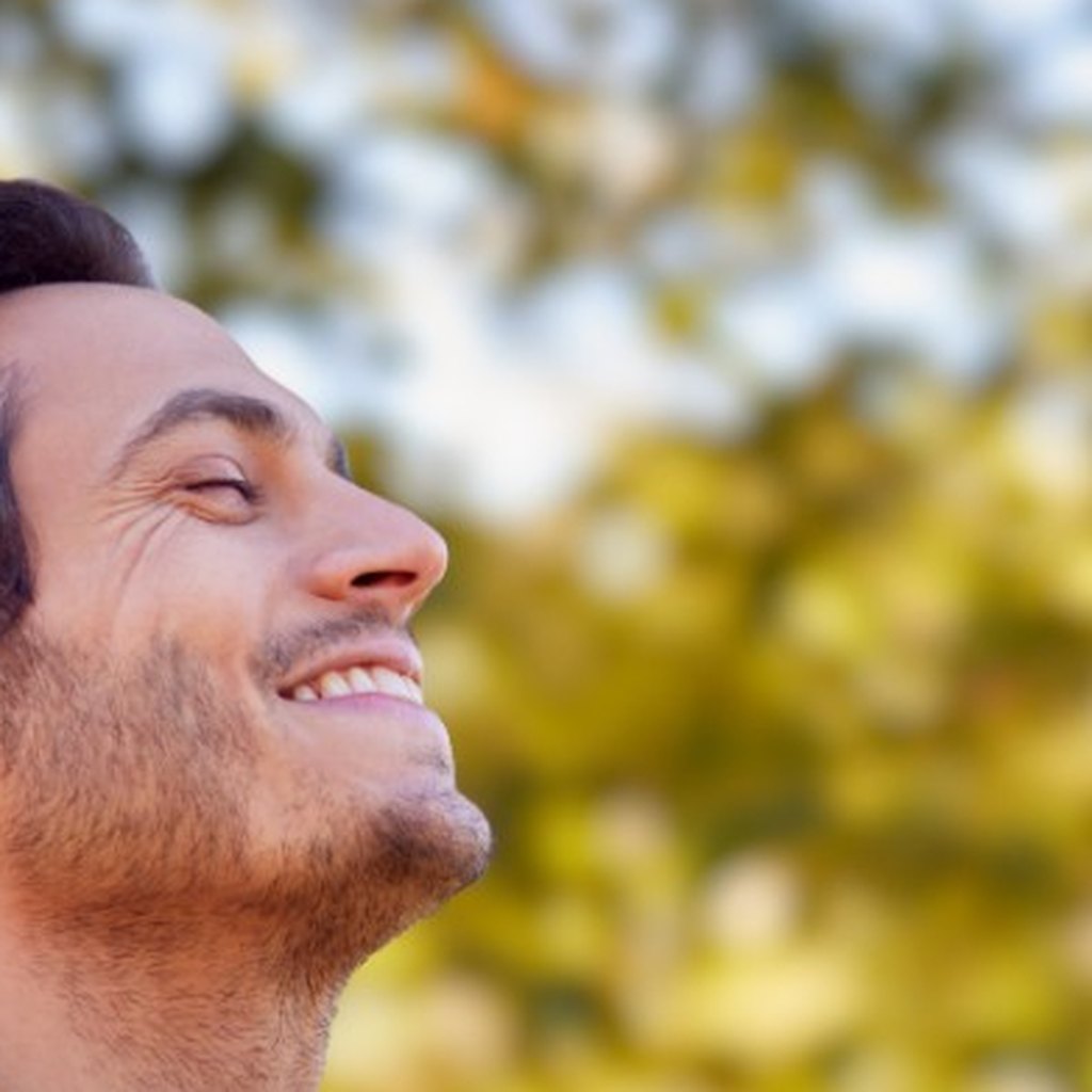 Man smiling with eyes closed outdoors among autumn trees