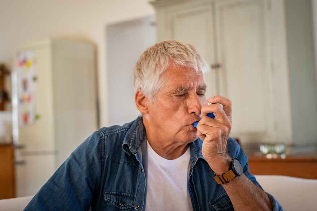 Older man using a blue inhaler at home