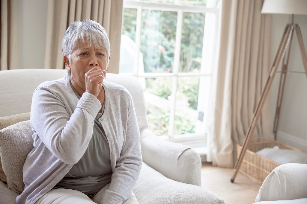Older woman coughing while seated at home