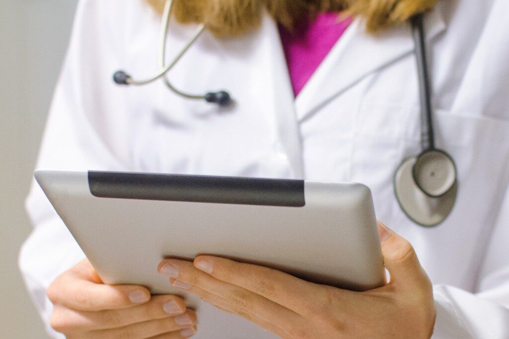 Healthcare professional in a white coat holding a tablet for a follow-up review